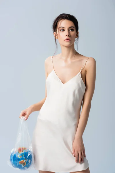 Брюнетка в шовковій сукні тримає поліетиленовий пакет з глобусом ізольовано на сірому, концепція екології — стокове фото