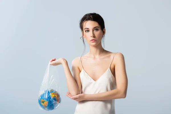 Young woman in silk dress holding plastic bag with globe isolated on grey, ecology concept — Stock Photo