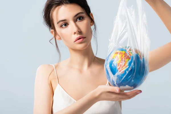 Young woman in silk dress holding plastic bag with globe isolated on white, ecology concept — Stock Photo