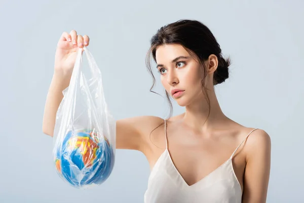 Mujer joven en vestido de seda mirando bolsa de plástico con globo aislado en blanco, concepto de ecología - foto de stock