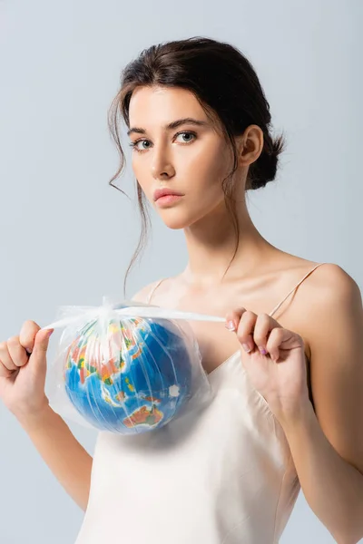 Jeune femme brune tenant un sac en plastique avec globe et regardant la caméra isolée sur blanc, concept d'écologie — Photo de stock