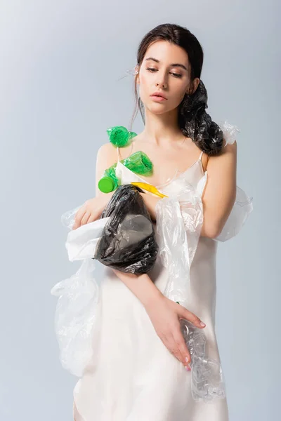 Brunette femme tenant des bouteilles vides et des sacs en plastique isolés sur gris, concept écologie — Photo de stock