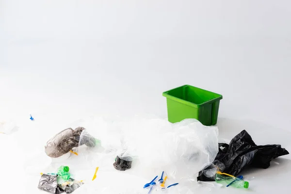 Bolsas de plástico, botellas y cucharas cerca de bote de basura en blanco, concepto de ecología - foto de stock