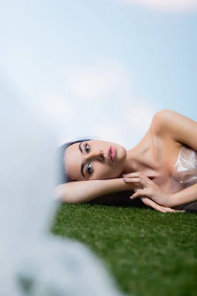 Selective focus of young model lying near polyethylene on grass, ecology concept — Stock Photo