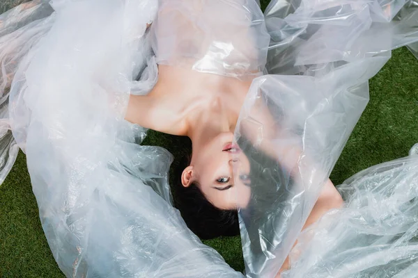 Top view of young model wrapped in polyethylene lying and looking at camera, ecology concept — Stock Photo