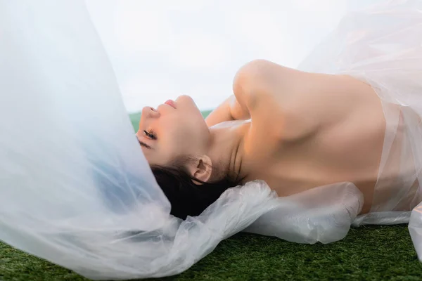 Modelo jovem envolto em polietileno deitado sobre branco, conceito de ecologia — Fotografia de Stock