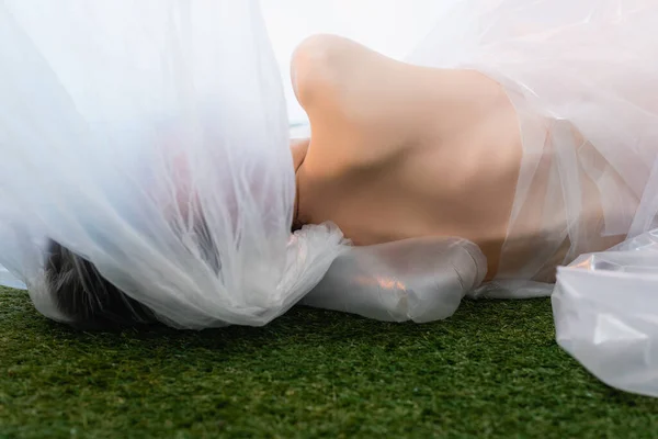 Vista trasera de la mujer desnuda acostada cerca de polietileno sobre hierba - foto de stock