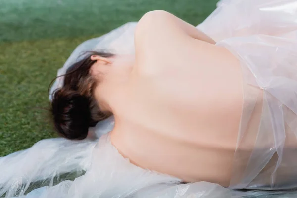 Vue arrière de la femme nue et brune couchée près de polyéthylène sur l'herbe — Photo de stock