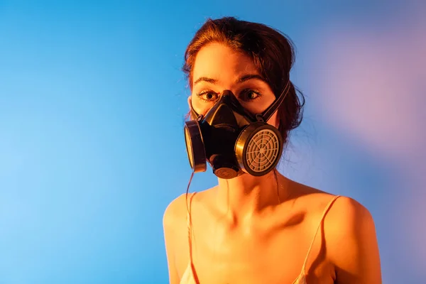 Brünettes Modell in Gasmaske mit Blick auf Kamera auf blau — Stockfoto