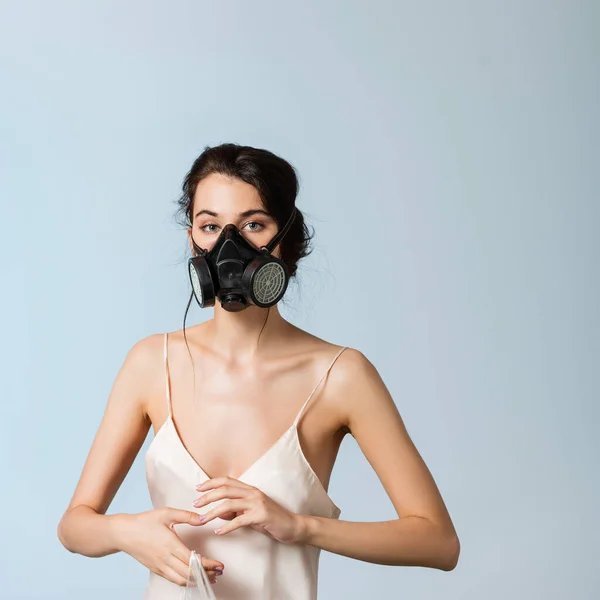 Joven morena en máscara de gas sosteniendo bolsa de plástico aislado en gris, concepto de ecología - foto de stock