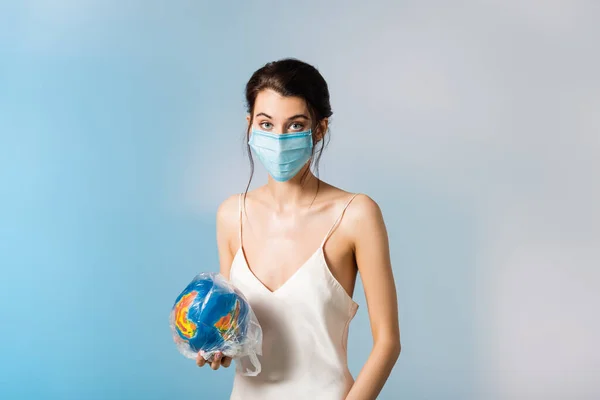Mulher em máscara médica segurando saco de plástico com globo em azul, conceito de ecologia — Fotografia de Stock