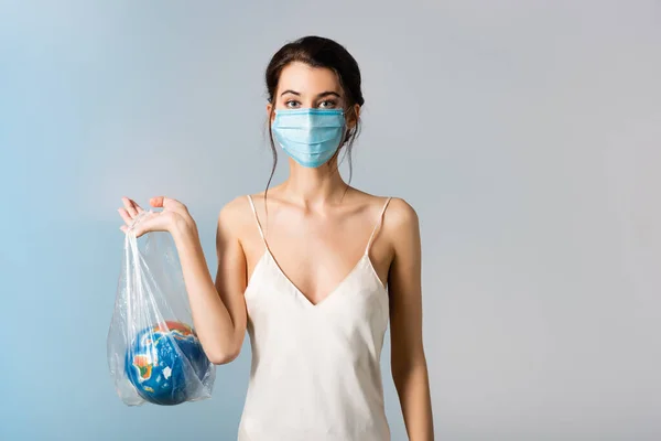 Young model in medical mask holding plastic bag with globe on blue, ecology concept — Stock Photo