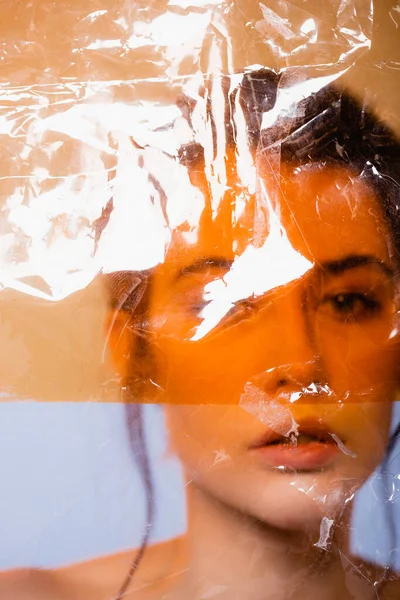 Young woman looking at camera through polyethylene on grey, ecology concept — Stock Photo