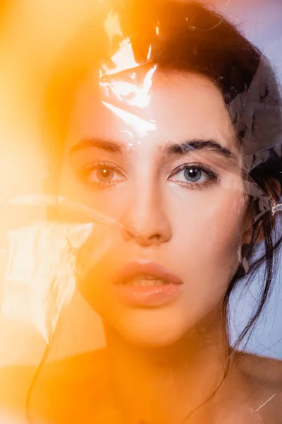 Naked woman looking at camera through polyethylene on grey, ecology concept — Stock Photo