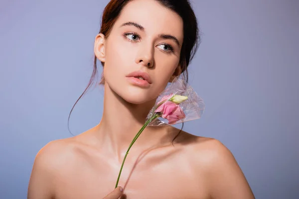Nackte junge Frau, die Blumen in Polyethylen hält und isoliert von grauen, ökologischen Konzepten wegsieht — Stockfoto