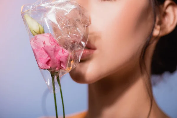 Abgeschnittene Ansicht einer jungen Frau mit Blumen in Polyethylen auf Grau, Ökologiekonzept — Stockfoto