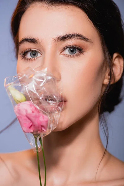 Brünette Frau mit Blumen in Polyethylen isoliert auf grau, ökologisches Konzept — Stockfoto