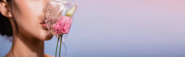 Горизонтальный урожай цветов в полиэтилене рядом с молодой женщиной на голубом, экологическая концепция — стоковое фото