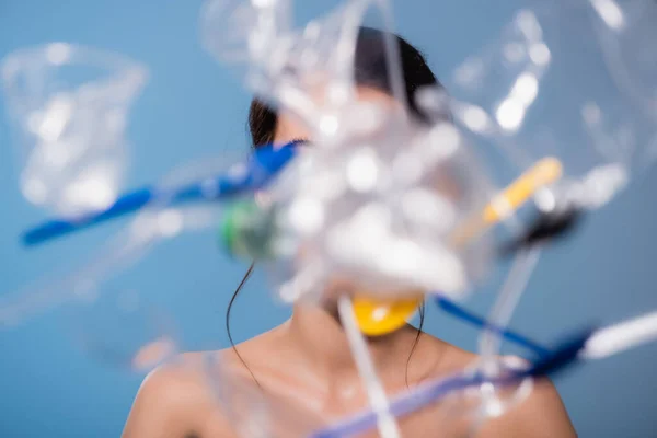 Enfoque selectivo de la mujer desnuda cerca de caer vasos de plástico, cucharas y tenedores en azul, concepto de ecología - foto de stock