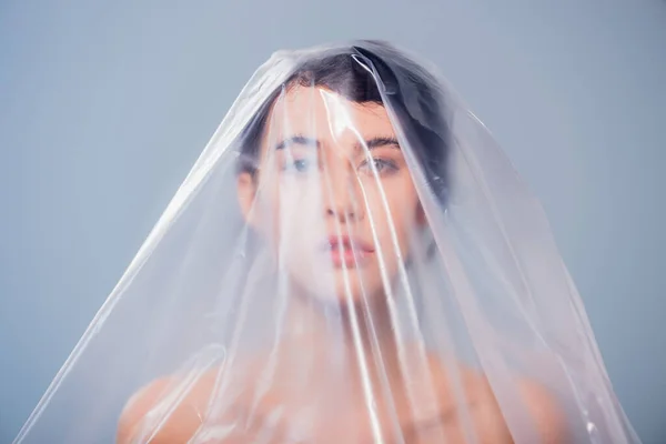 Brunette model covered with polyethylene looking at camera isolated on grey, ecology concept — Stock Photo