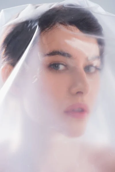 Молодая брюнетка, покрытая полиэтиленом, смотрящая на камеру, экологическая концепция — стоковое фото