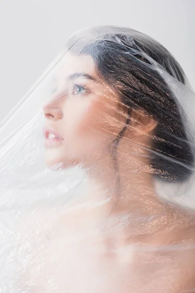 Mujer morena cubierta de polietileno mirando hacia arriba aislado en gris, concepto de ecología - foto de stock