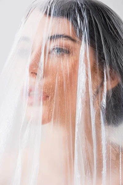 Junge brünette Frau schaut weg durch Polyethylen isoliert auf grau, ökologisches Konzept — Stockfoto