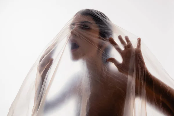 Trapped brunette woman screaming through polyethylene isolated on white, ecology concept — Stock Photo