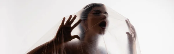 Horizontal concept of brunette woman screaming through polyethylene isolated on white, ecology concept — Stock Photo