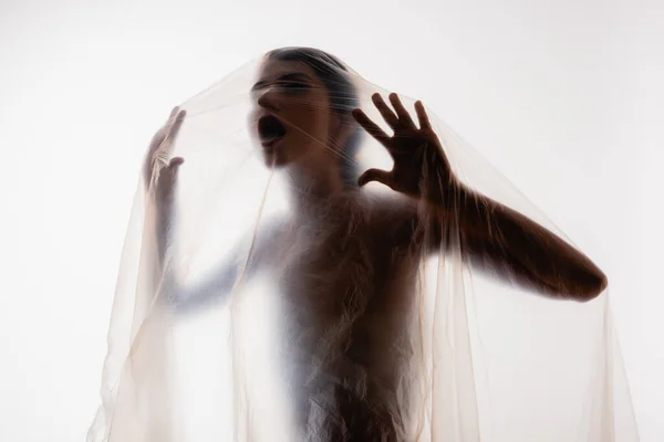 Joven mujer atrapada gritando a través de polietileno aislado en blanco, concepto de ecología — Stock Photo
