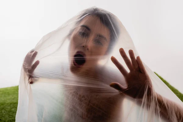 Morena mujer gritando a través de polietileno en blanco, concepto de ecología - foto de stock