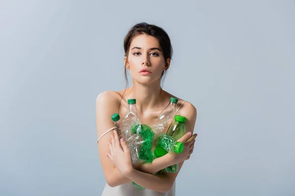 Morena mujer mirando a la cámara y sosteniendo botellas de plástico aisladas en gris, concepto de ecología - foto de stock