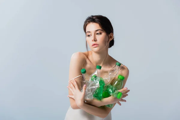 Brunette woman looking away and holding plastic bottles isolated on grey, ecology concept — Stock Photo