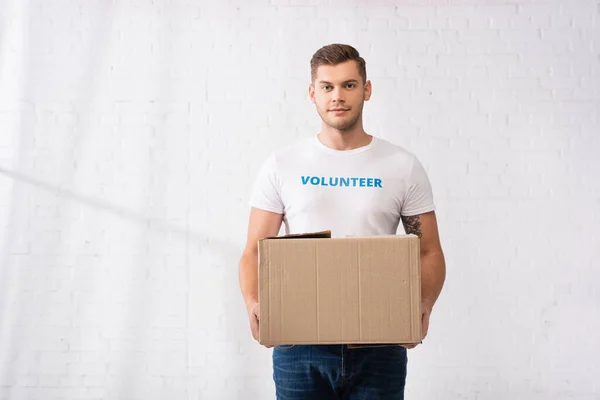 Volunteer with lettering on t-shirt looking at camera while holding carton package — Stock Photo