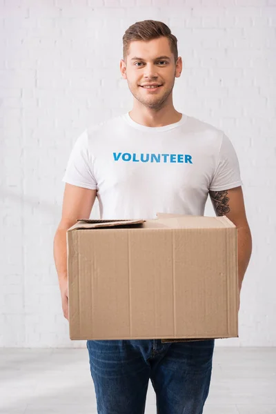 Voluntário em t-shirt branca segurando pacote de papelão no centro de caridade — Fotografia de Stock