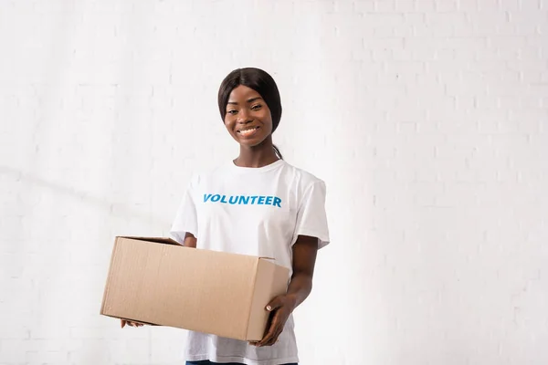 Giovane volontario afroamericano con scatola di cartone che guarda la macchina fotografica nel centro di beneficenza — Foto stock