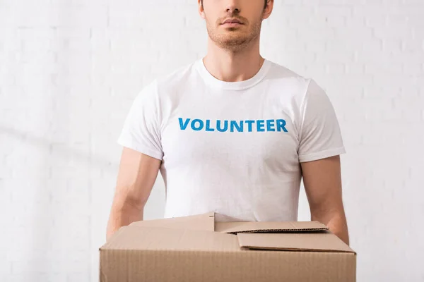 Vista recortada del voluntario en camiseta con letras que sostiene la caja de cartón - foto de stock