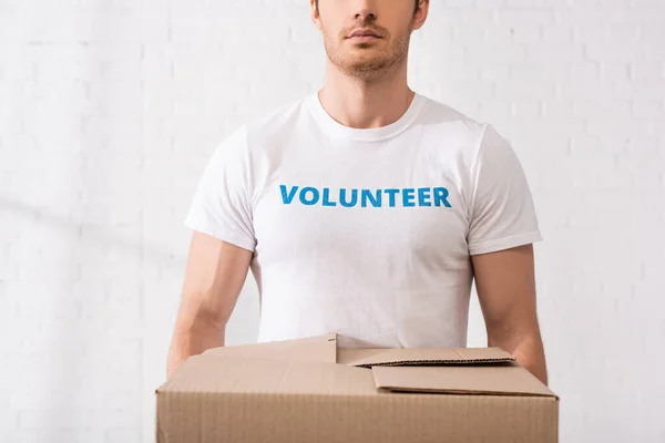 Vista recortada del voluntario en camiseta con letras que sostiene la caja de cartón - foto de stock