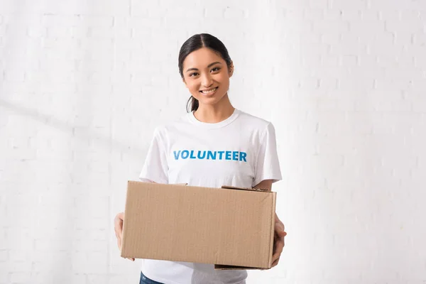 Voluntario asiático con letras en camiseta que sostiene el paquete en el centro de caridad - foto de stock