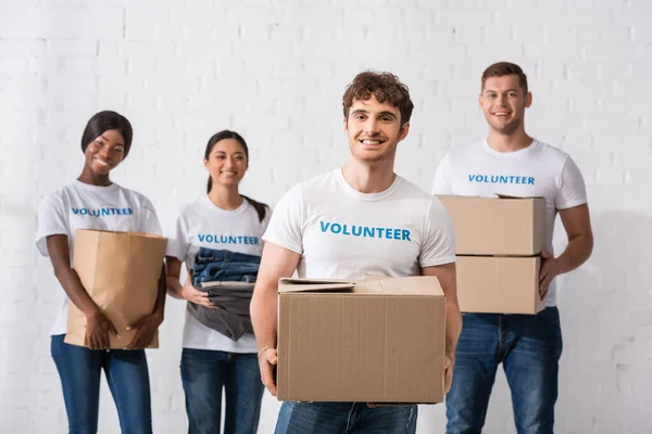 Selective focus of man with package standing near multiethnic volunteers in charity center — Stock Photo