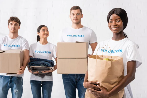 Enfoque selectivo del voluntario afroamericano sosteniendo bolsa de papel en centro de caridad - foto de stock