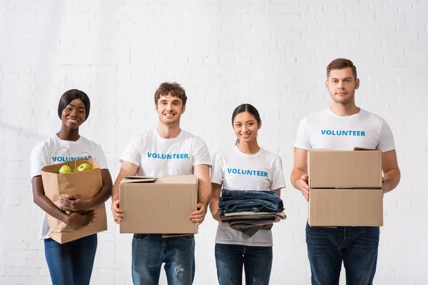 Volontari multiculturali con scritte su t-shirt contenenti pacchi e vestiti nel centro di beneficenza — Foto stock