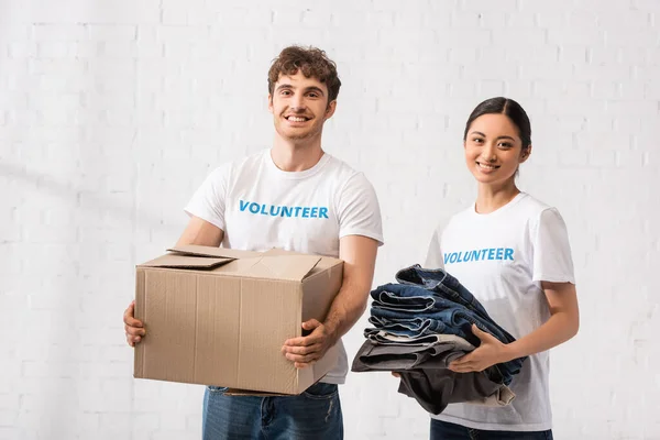 Voluntários multiculturais segurando pacote e roupas no centro de caridade — Fotografia de Stock