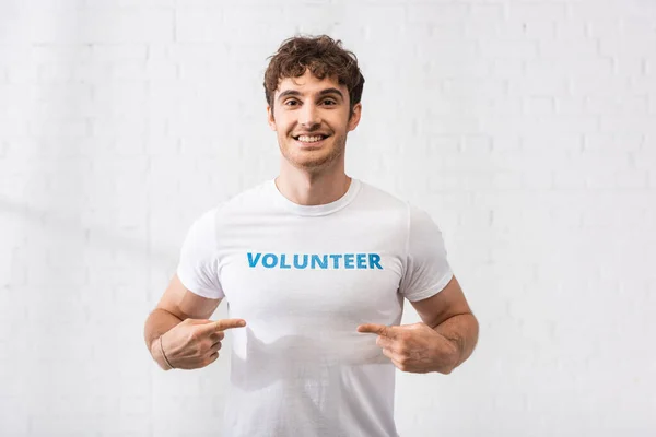 Junger Mann zeigt mit dem Finger auf freiwilligen Schriftzug auf T-Shirt — Stockfoto
