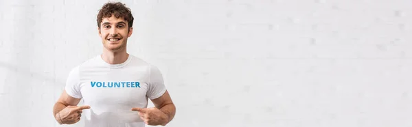 Panoramic shot of man pointing at t-shirt with volunteer lettering — Stock Photo