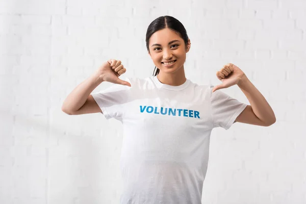Voluntarios asiáticos señalando con los dedos las letras en la camiseta - foto de stock