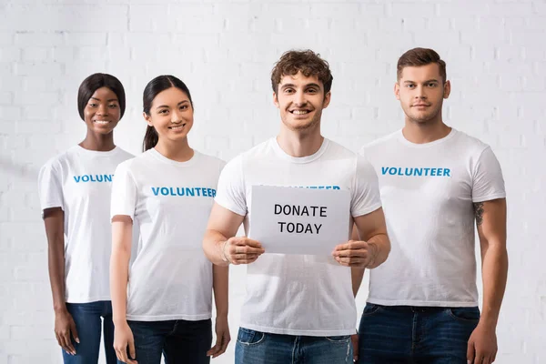 Selective focus of man holding card with donate today lettering near multicultural volunteers — Stock Photo