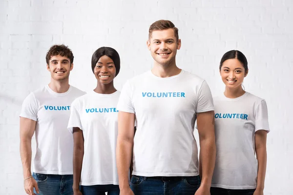 Jóvenes voluntarios multiétnicos en camisetas con letras mirando a la cámara en el centro de caridad - foto de stock