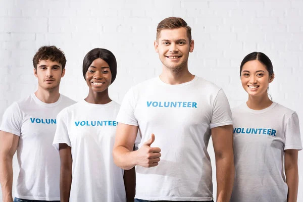 Enfoque selectivo del hombre mostrando gesto de aprobación cerca de voluntarios multiculturales - foto de stock