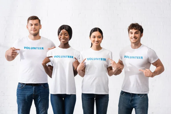 Multiethnic volunteers pointing with fingers at lettering on t-shirts — Stock Photo